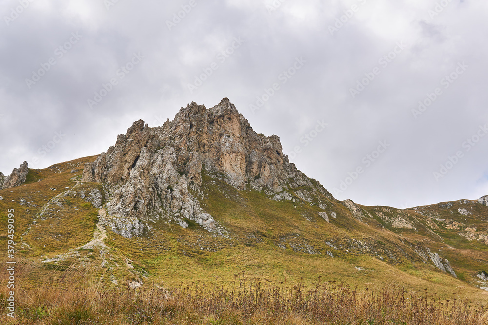 Obraz premium beautiful rocky cliff on a mountain ridge in the distance and an autumn alpine meadow in the foreground