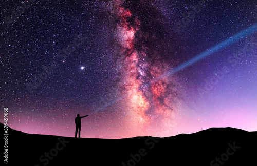 Beautiful starry sky with bright milky way galaxy. Night landscape . Person silhouette stands on the shore with flashlight illuminate starry sky.