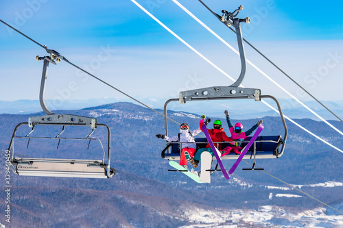 Photography Fun team of friends skier and snowboarders up ski lift on blue sky background