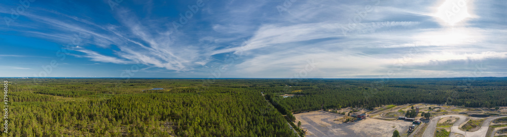 Breathtaking Aerial View of Endless Scandinavian green pine tree forest up to horizon line, speedway training track at right side. Sunny summer day, Typical Northern Scandinavia landscape