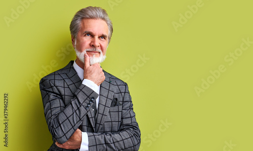 portrait of pleasant senior businessman in stylish suit isolated in studio, green background. gray bearded male is successful enrepreneur, posing photo