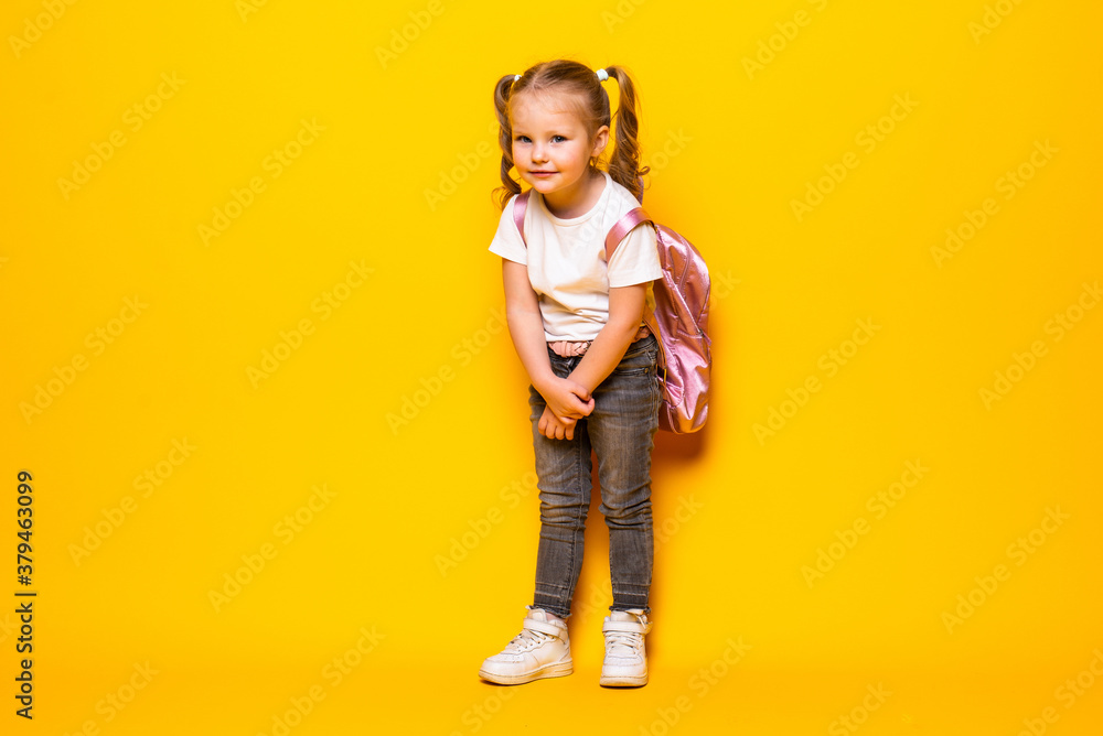 Portrait of smiling little schoolgirl with backpack on yellow background