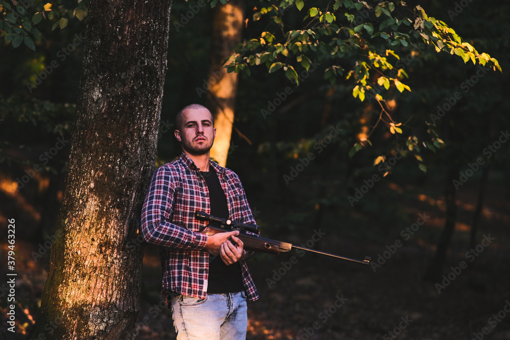 Charismatic guy in a checkered shirt with a weapon. In the autumn forest. Home protection alone