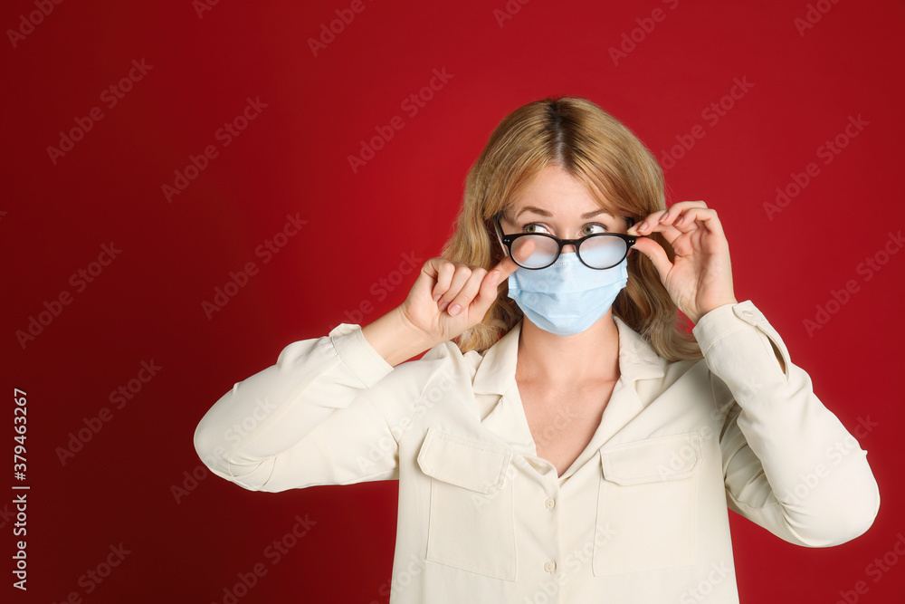 Woman wiping foggy glasses caused by wearing medical mask on red background Woman wiping foggy glasses caused by wearing medical mask on red background