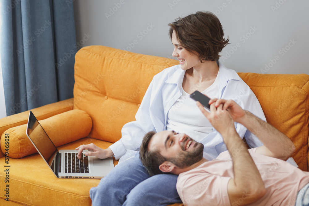 Funny smiling young couple two friends man woman 20s wearing casual clothes  sitting lying on couch