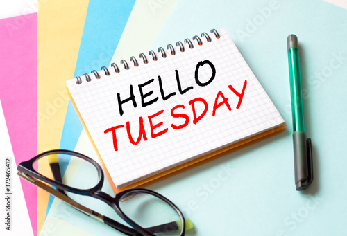 The Notepad with the text Hello Tuesday is on colored paper with glasses and a pen