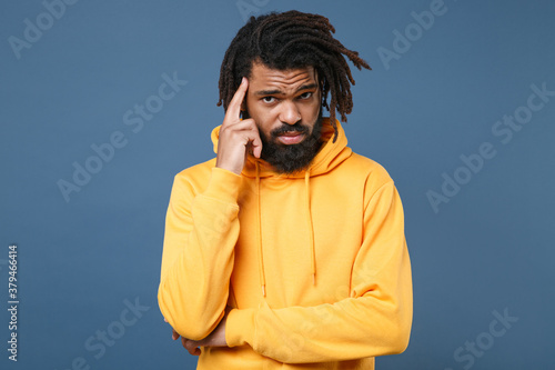 Pensive puzzled young african american man guy wearing yellow streetwear hoodie posing isolated on blue wall background studio portrait. People sincere emotions lifestyle concept. Put hand on head.