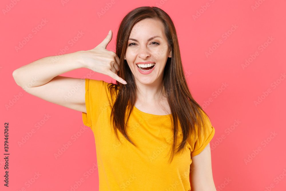 Cheerful laughing young brunette woman 20s in yellow casual t-shirt posing standing doing phone gesture like says call me back looking camera isolated on pink color wall background studio portrait. Cheerful laughing young brunette woman 20s in yellow casual t-shirt posing standing doing phone gesture like says call me back looking camera isolated on pink color wall background studio portrait.