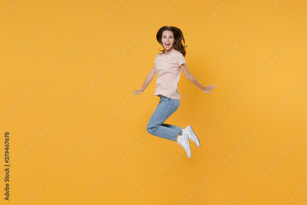 Full length side view portrait of excited cheerful funny young woman 20s wearing pastel pink casual t-shirt posing jumping spreading hands looking camera isolated on yellow color background studio.