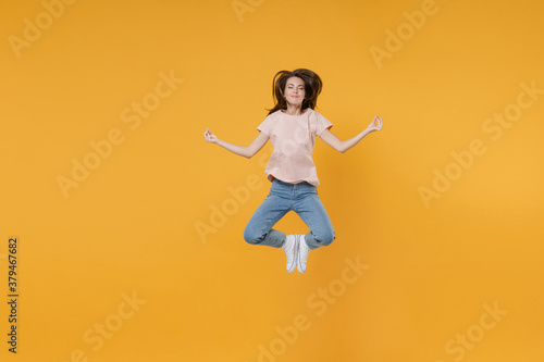 Full length portrait of smiling young woman 20s in pastel pink casual t-shirt jumping hold hands in yoga gesture, relaxing meditating, trying to calm down isolated on yellow color background studio.