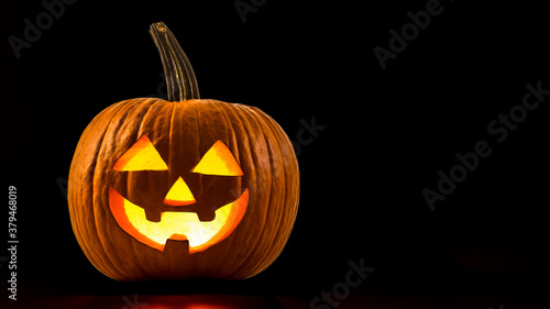 Carved Pumpkin on Halloween. Jack O Lantern smile face. Illuminating with burning candle inside. Decoration from pumpkins. Scary Jack-o'-Lantern face. Happy Halloween. Black background with copy space