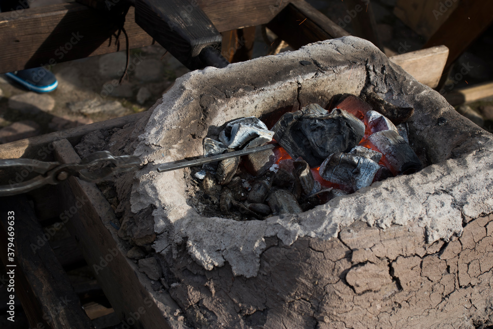 blacksmith sets up the brazier with embers with large coal tongs. Embers glow in a iron forge. Fire, heat, coal and ash blacksmith sets up the brazier with embers with large coal tongs. Embers glow in a iron forge. Fire, heat, coal and ash