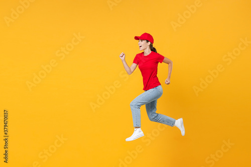 Full length body fun delivery employee woman in red cap blank t-shirt uniform work courier in service during quarantine coronavirus covid-19 virus jumping isolated on yellow background studio portrait