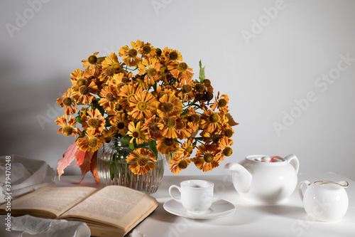 bouquet of orange helenium with wild grape leaves in a fluted glass vase against a dark blue wall. photo
