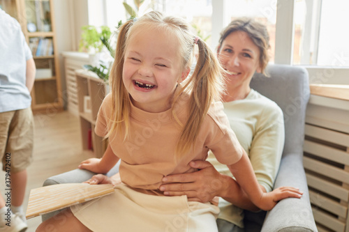 Portrait of cute girl with down syndrome laughing happily while playing with mother at home photo
