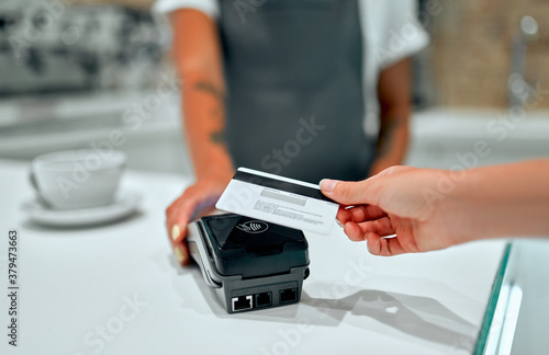 Young attractive female barista stands at the counter in a coffee shop. Customer paying for their order with a credit card in a cafe.