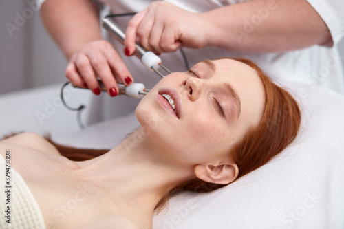 20-25 years old woman receiving a non-surgical rejuvenation procedure  RF face lifting with the use of electric device equipment. hardware facial massage