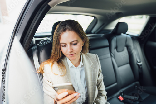 Businesswoman using smartphone while traveling by car on the backseat. Business lady looking on phone and typing text © leonidkos