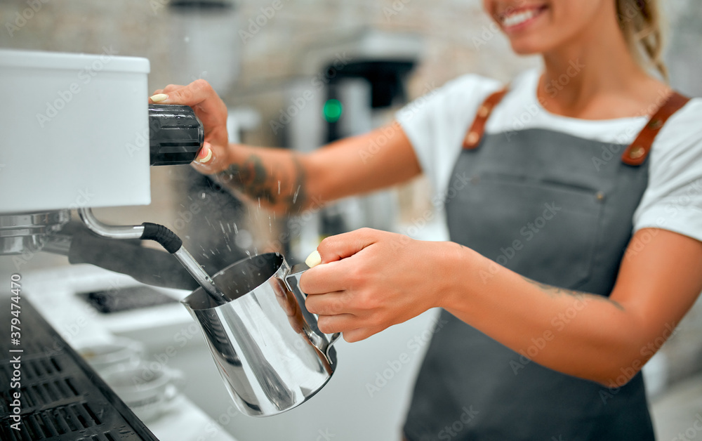 Young attractive woman barista prepares coffee in a coffee shop.