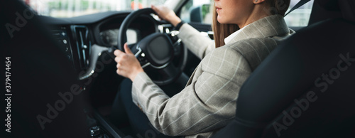 Business woman driving modern car. Young businesswoman traveling by car while sit behind the wheel. Wide shot photo