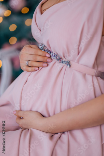 belly of a pregnant girl in an air blush pink dress, close-up. New Year's photo session in anticipation of the child.