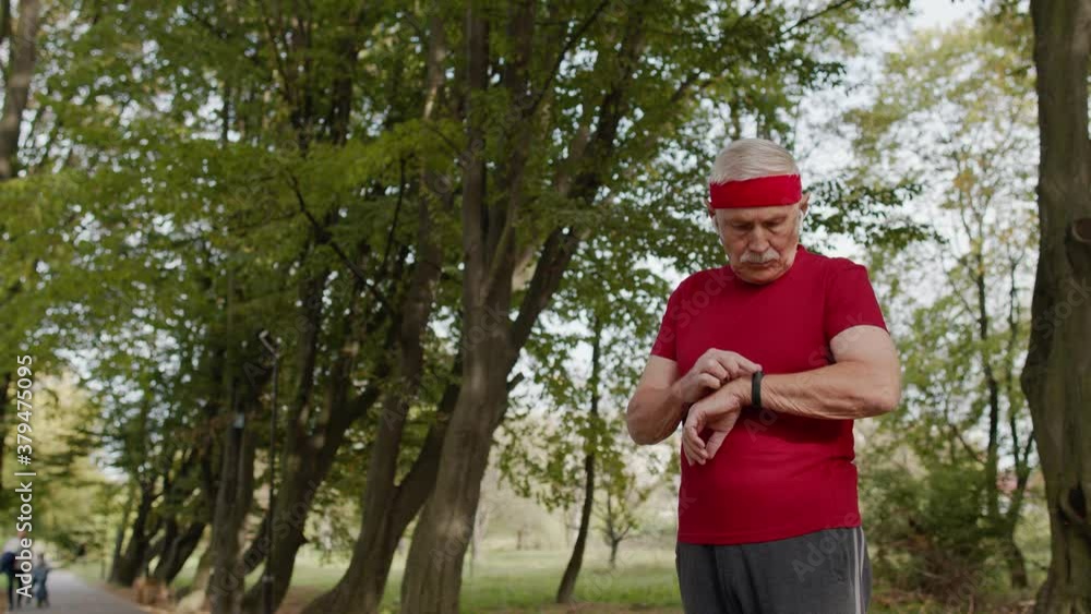 Senior runner man in park using smart watch, tracking distance, checking pulse after fitness workout Senior runner man in park using smart watch, tracking distance, checking pulse after fitness workout