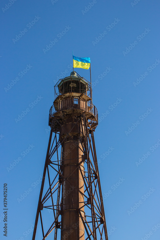 Old steel lighthouse with Ukrainian national flag on top. Abandoned lighthouse on island, Ukraine. Patriotism concept. Marine navigation. Maritime concept. Summer tourism in Ukraine. Naval navigation. Old steel lighthouse with Ukrainian national flag on top. Abandoned lighthouse on island, Ukraine. Patriotism concept. Marine navigation. Maritime concept. Summer tourism in Ukraine. Naval navigation.