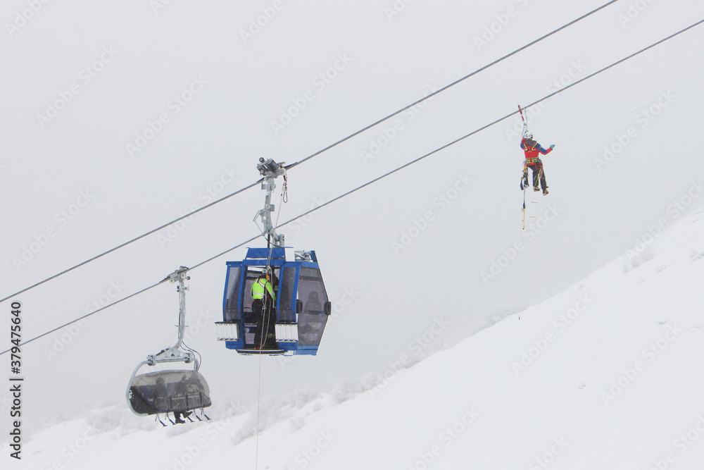 Heroes rescue teams on a chairlift at ski resort on the Dolomites. Emergency rescue passengers with the use of ropes and safety ladders in bad weather winter conditions. Foggy day. 