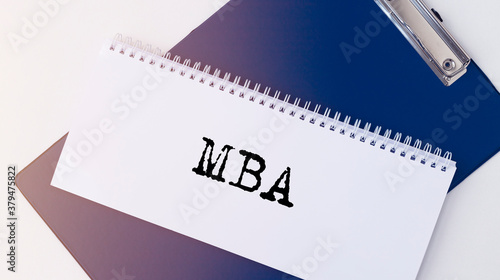 Business educatuion concept. white spiral notebook with text MBA acronym on office table on blue board, flatlay, master of business administration photo