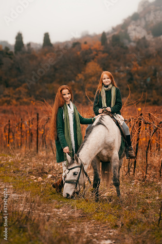 A young woman and a girl with red long hair walk in the wineries in the fall and ride horses.