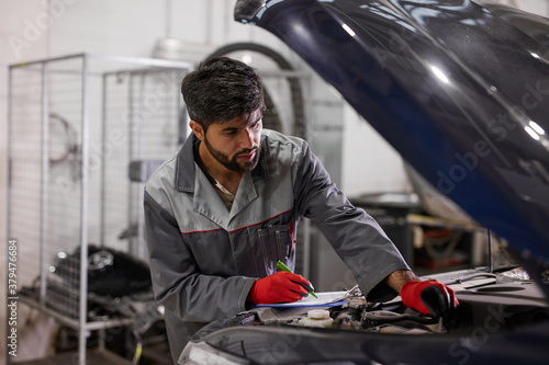 caucasian concentrated auto mechanic man check the hood of car, make notes