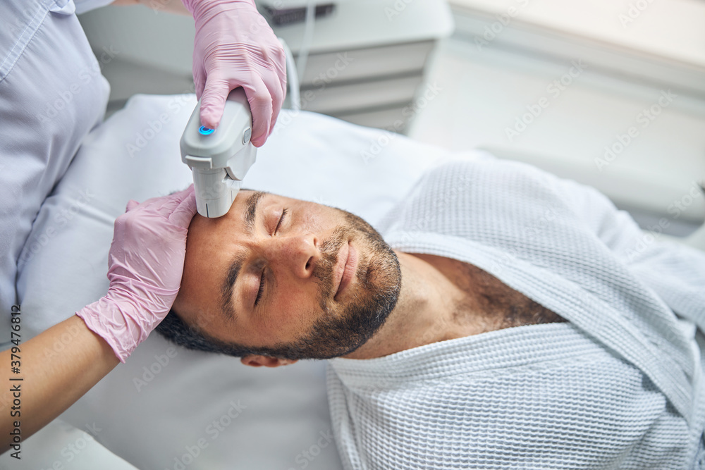 Female esthetician treating male skin with laser device Female esthetician treating male skin with laser device