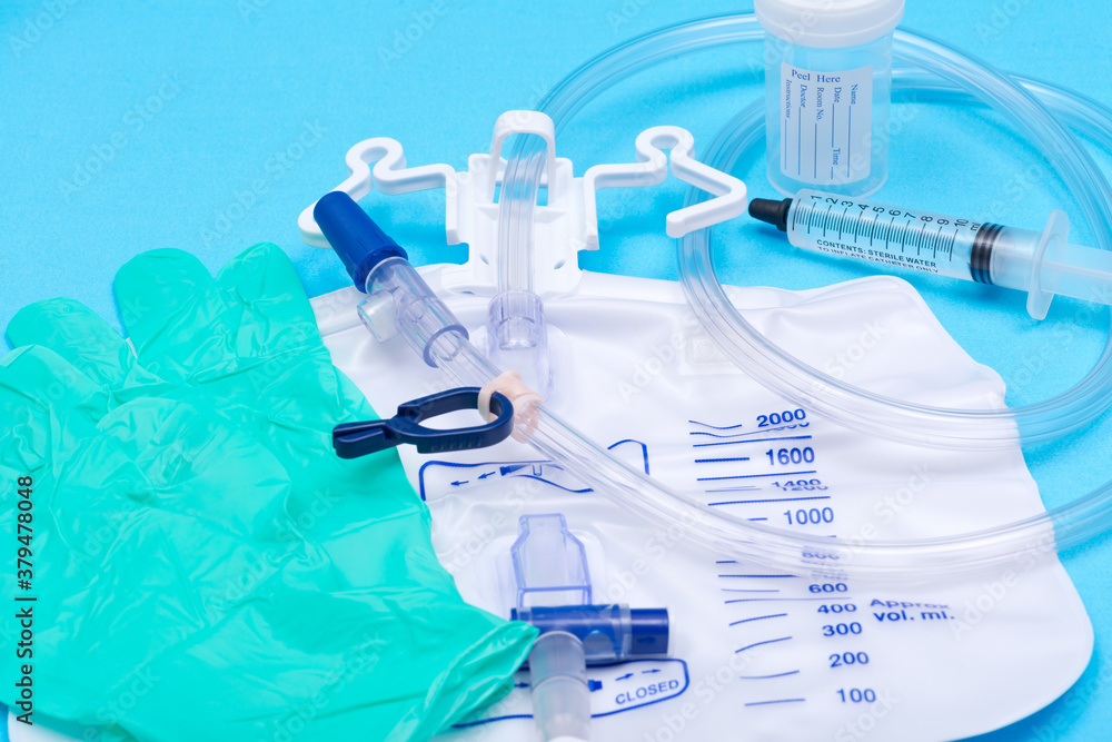 Fototapeta premium Sterile urinary drainage bag, 10 ml syringe pre-filled with sterile water and specimen container with lid and label. Isolated on blue background.