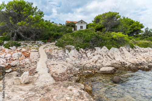 Rocky shore and path leading to a village on a hill on the island of Lavsa in the Adriatic sea in Croatia photo