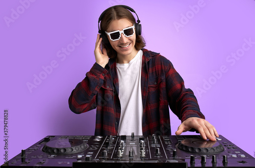 caucasian stylish dj man in sunglasses mixing console on purple studio background, perform dance club music. portrait