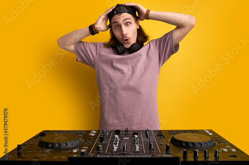 young caucasian dj man perform music with the use of special equipment, long haired male in casual wear have fun, wearing headphones. music, dj concept. studio shoot