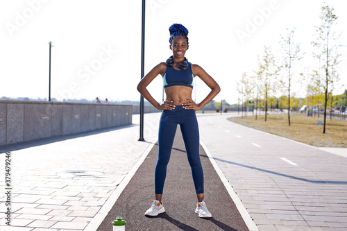 portrait of smiling african woman standing outdoors, after sport exercises, look at camera and smile photo