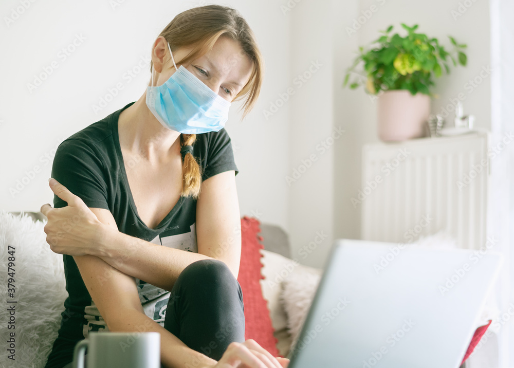 Woman with medical face mask at home using laptop. Woman with medical face mask at home using laptop.