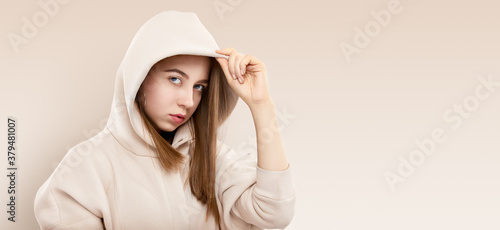 Stylish pretty cool funky teen girl in light sweatshort with hood. Girl teenager wearing trendy hoodie casual clothes. Strong face and long hair. Studio portrait of femle youngster urban style.