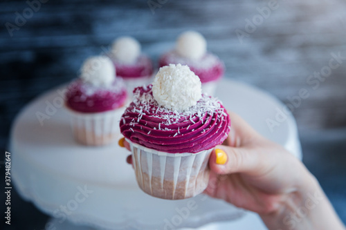 Female hand takes from the stand a delicious cupcake with violet cream decorated with balls topped with coconut crumbs
