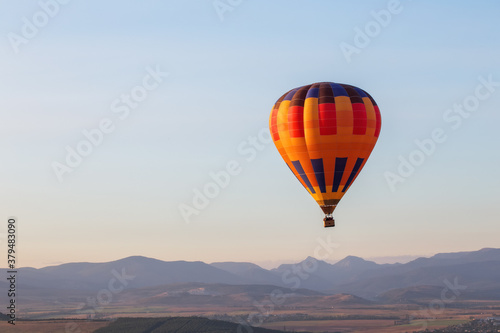 Hot air balloon in the blue sky. Mountains in the background.