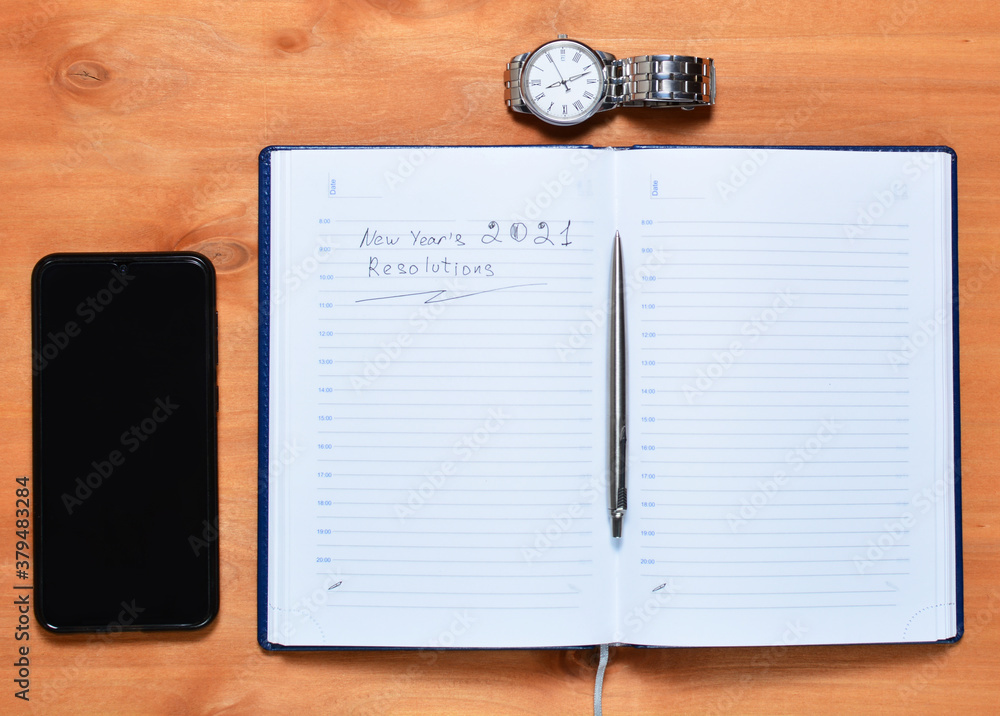 top view of a notebook with a pen smartphone and a clock, new goals in the coming year. wooden background.