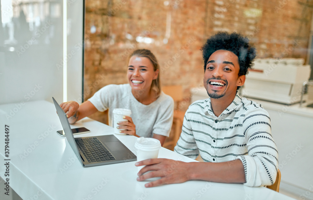 A beautiful woman and an attractive African man are drinking coffee in a coffee shop, working on a laptop, chatting and having fun. A beautiful woman and an attractive African man are drinking coffee in a coffee shop, working on a laptop, chatting and having fun.