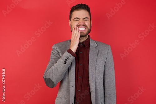 Young caucasian businessman wearing casual clothes standing over isolated red background touching mouth with hand with painful expression because of toothache or dental illness on teeth.