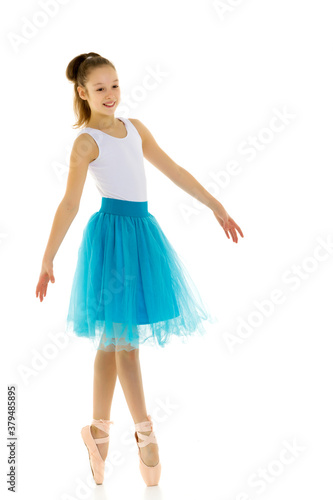 Cute little girl in a tutu and pointe shoes dancing in the studio on a white background. © lotosfoto
