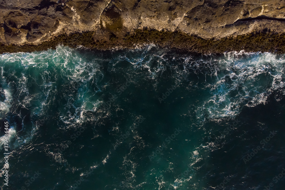 Obraz premium Aerial view of ocean waves and fantastic Rocky coast. Blue water background. The rocky coast is on top on the photo. Wallpaper. Raging ocean.