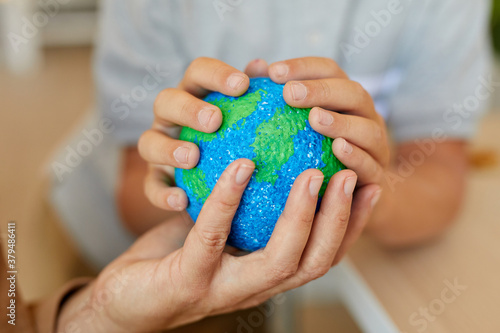 Close up of unrecognizable child holding planet model while studying at home with mother or tutor ,copy space