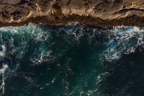 Aerial view of ocean waves and fantastic Rocky coast. Blue water background. The rocky coast is on top on the photo. Wallpaper. Raging ocean.