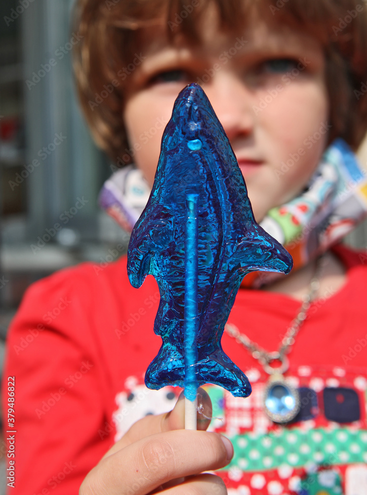 Naklejka premium Blue fish-shape lollipop on the foreground, a child holding it on the background.