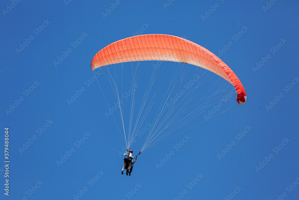 Blue Paraglider tandem instructor with a tourist flying into the sky with clouds on a sunny day Blue Paraglider tandem instructor with a tourist flying into the sky with clouds on a sunny day
